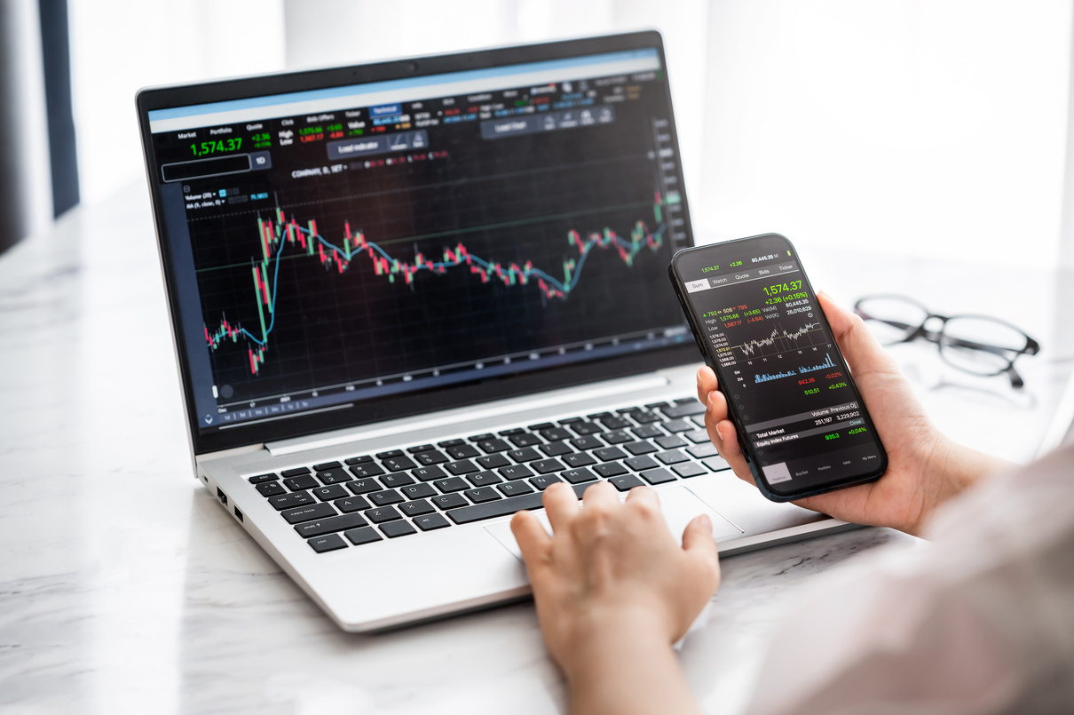 Person Using Smartphone and Laptop for Trading Stocks Online